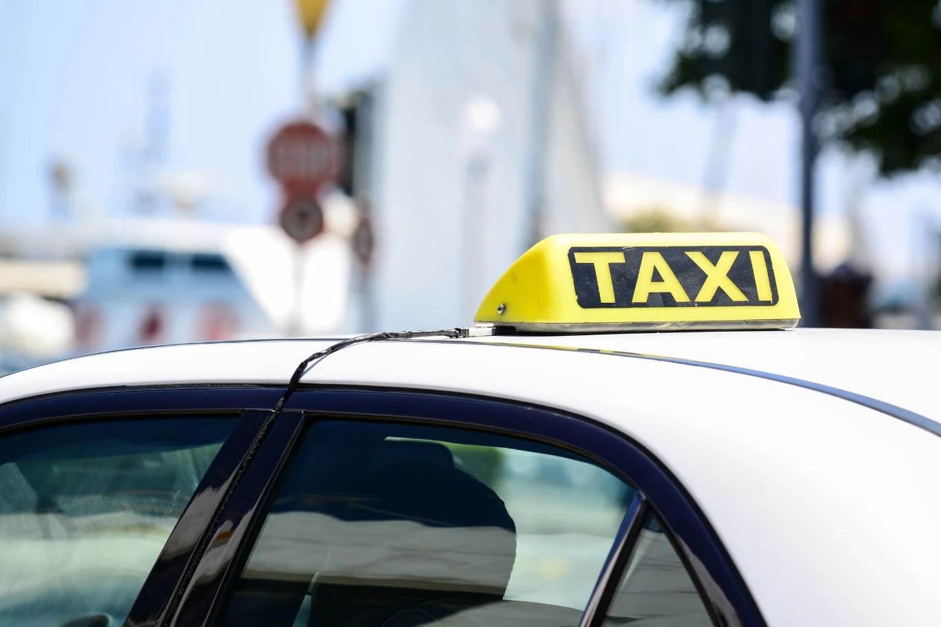 Czy w Uberze dziecko powinno siedzieć w foteliku? Żółty znak TAXI na dachu białego samochodu z widoczną górną częścią pojazdu i rozmytym miejskim tłem w słoneczny dzień