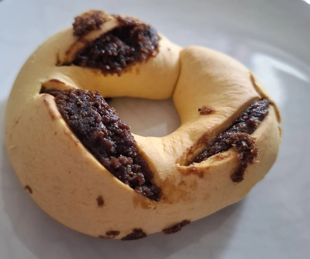 Qagħaq tal-għasel, krążki miodowe Okrągłe ciastko z jasnym, kruchym ciastem z widocznymi trzema nacięciami wypełnionymi ciemnym nadzieniem, leżące na białym talerzu.
