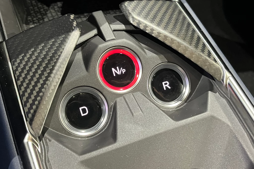 Panel sterowania automatycznej skrzyni biegów w samochodzie, z trzema przyciskami oznaczonymi literami D, N/P i R oraz elementami wykonanymi z karbonu.