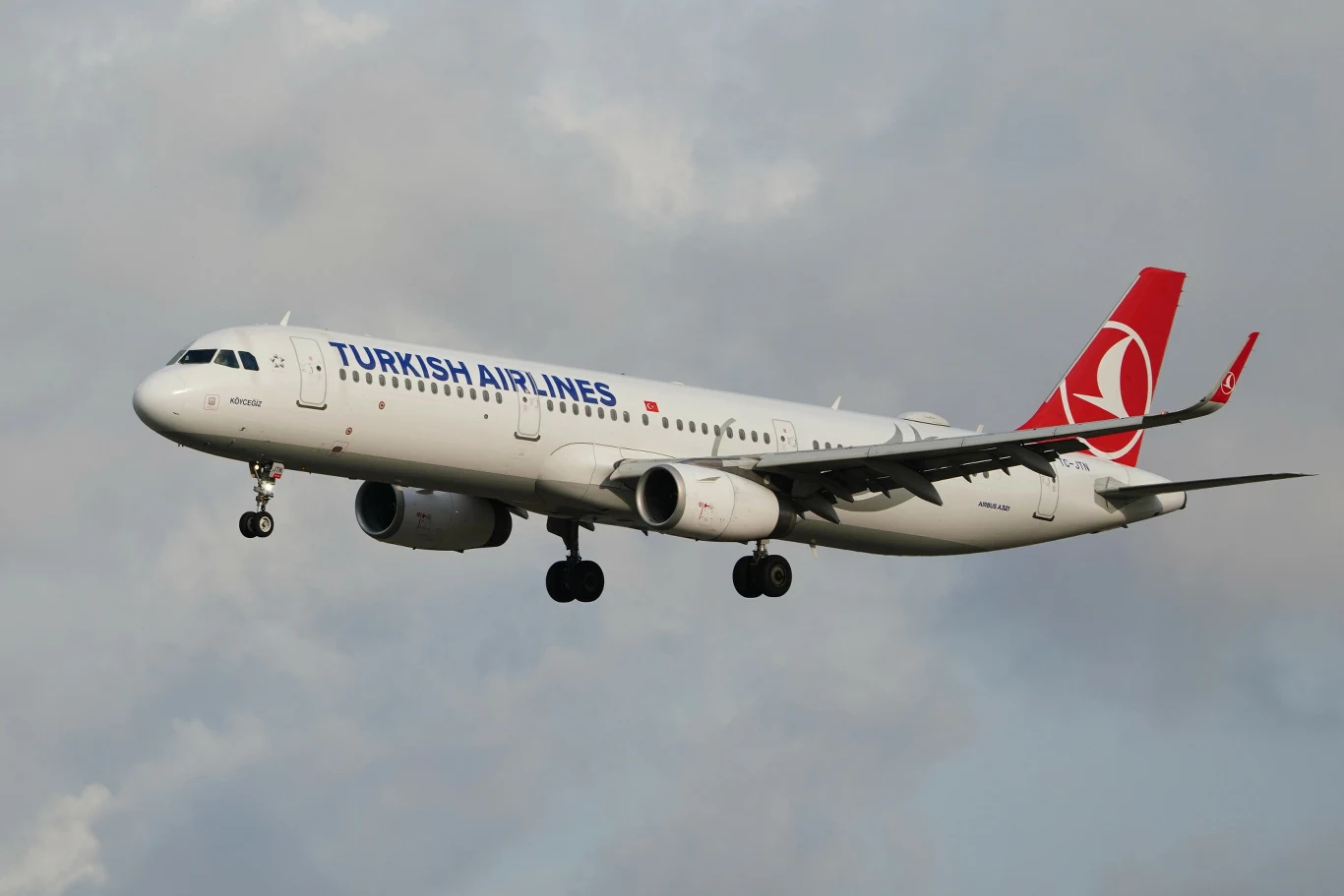 Samolot Turkish Airlines lądujący w Stambule. Samolot pasażerski Turkish Airlines w locie na tle pochmurnego nieba, widoczny w całości, z wysuniętym podwoziem i wyraźnie oznakowanym logotypem linii lotniczych na ogonie.