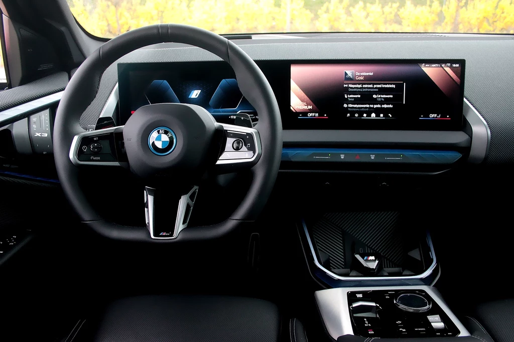 W kabinie BMW X3 dominują dwa ekrany ukryte pod jedną taflą szkła Kokpit nowoczesnego samochodu BMW z cyfrowym wyświetlaczem za kierownicą, dużym ekranem multimedialnym na środku deski rozdzielczej oraz stylowym panelem sterowania i dźwignią zmiany biegów.