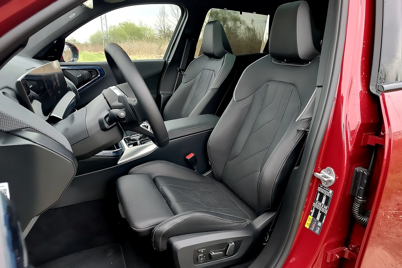 Luksusowe wnętrze samochodu z czarnymi, skórzanymi fotelami i nowoczesną deską rozdzielczą, dobrze widoczna kierownica oraz elementy sterowania po stronie kierowcy, drzwi szeroko otwarte.