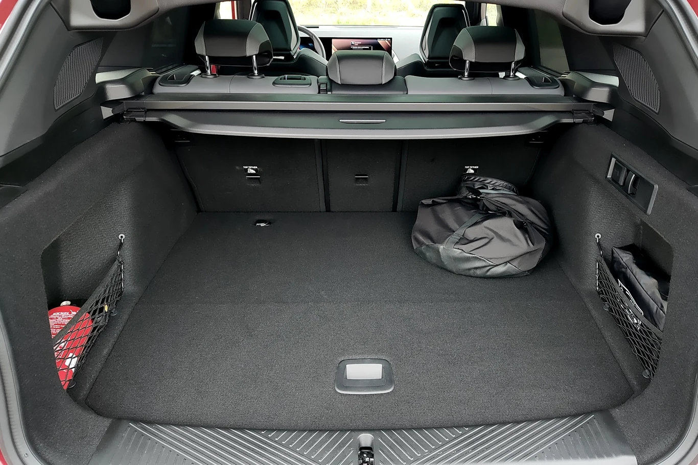 Obszerna, czysta przestrzeń bagażnika samochodowego z czarnym wnętrzem, składanymi tylniami siedzeniami, siatkami bocznymi oraz kilkoma drobnymi przedmiotami w środku, w tym torbą.