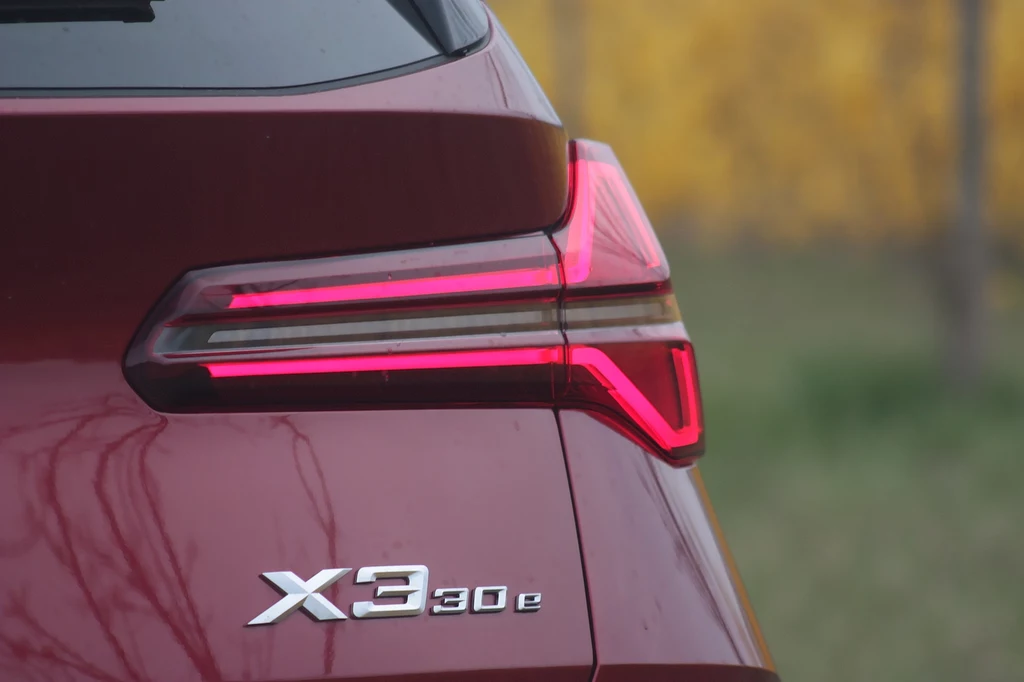 BMW X3 30e Tylna lampa samochodu BMW X3 30e w bordowym kolorze z wyraźnie widocznym oznaczeniem modelu oraz świecącym czerwonym światłem pozycyjnym.