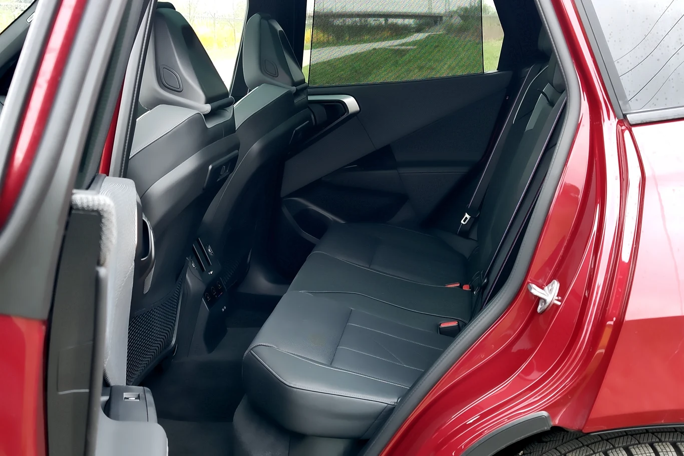 Wnętrze tylnej części czerwonego samochodu z otwartymi drzwiami, ciemne skórzane siedzenia tylnej kanapy, nowoczesna stylistyka i dużo miejsca na nogi dla pasażerów.