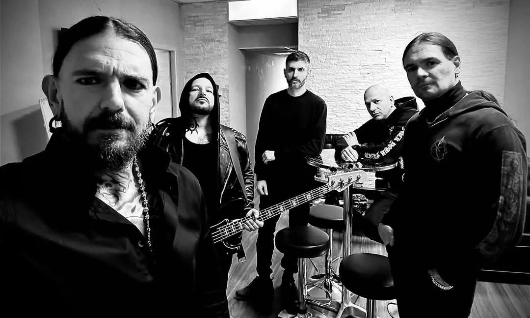 Beheaded przed premierą Pięciu mężczyzn w rockowym stylu stoi w pomieszczeniu, jeden z nich trzyma gitarę basową, pozostali przy okrągłym stole i krzesłach barowych, całość utrzymana w klimacie czarno-białej fotografii.