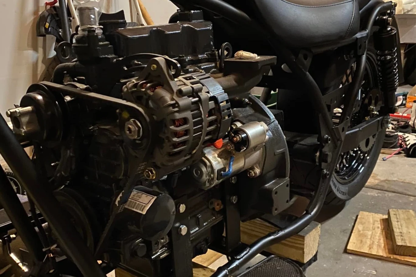 Silnik Diesla nie powala mocą, a dodatkowo jest cięższy i większy od jednostki benzynowej. Silnik zamontowany na ramie motocykla, widoczne szczegóły konstrukcyjne oraz elementy mechaniczne, całość ustawiona na drewnianych klockach na podłodze warsztatu.