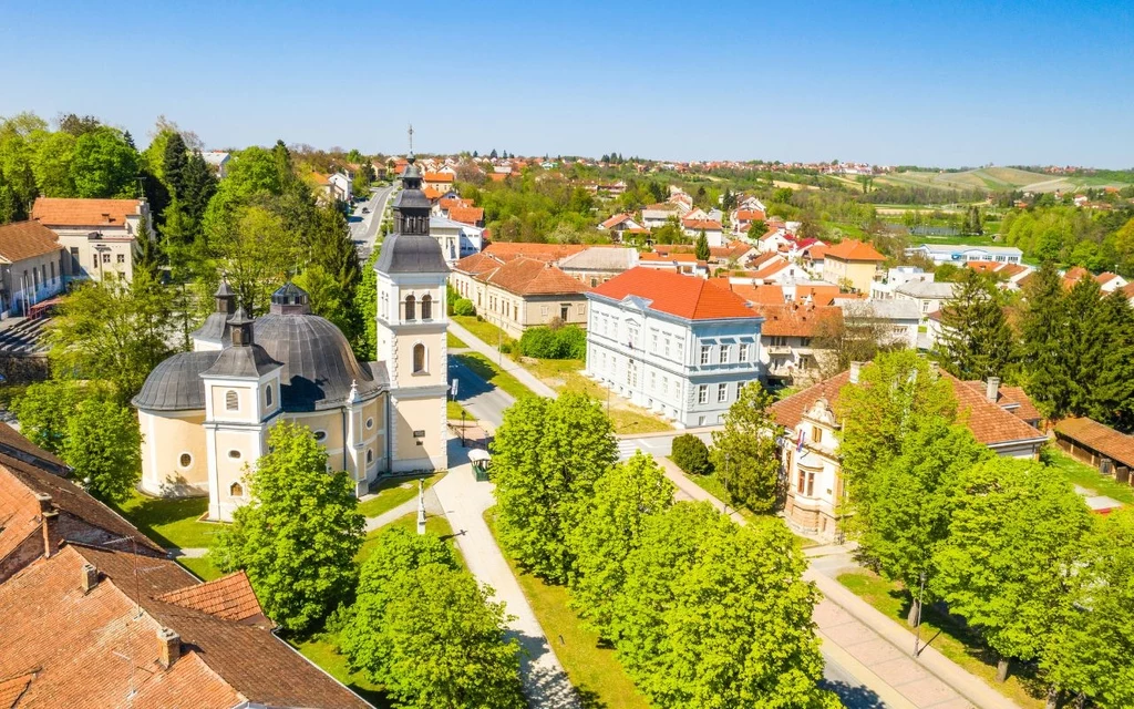 Slavonia może spodobać się turystom, którzy chcą uciec od ruchliwych ulic Centralnym punktem kompozycji jest okazały, jasny kościół otoczony bujną zielenią oraz szeroką aleją obsadzoną drzewami, w tle widać historyczną zabudowę miasteczka z przeważającymi dachami w odcieniach czerwieni oraz rozciągającymi się polami i zielon...