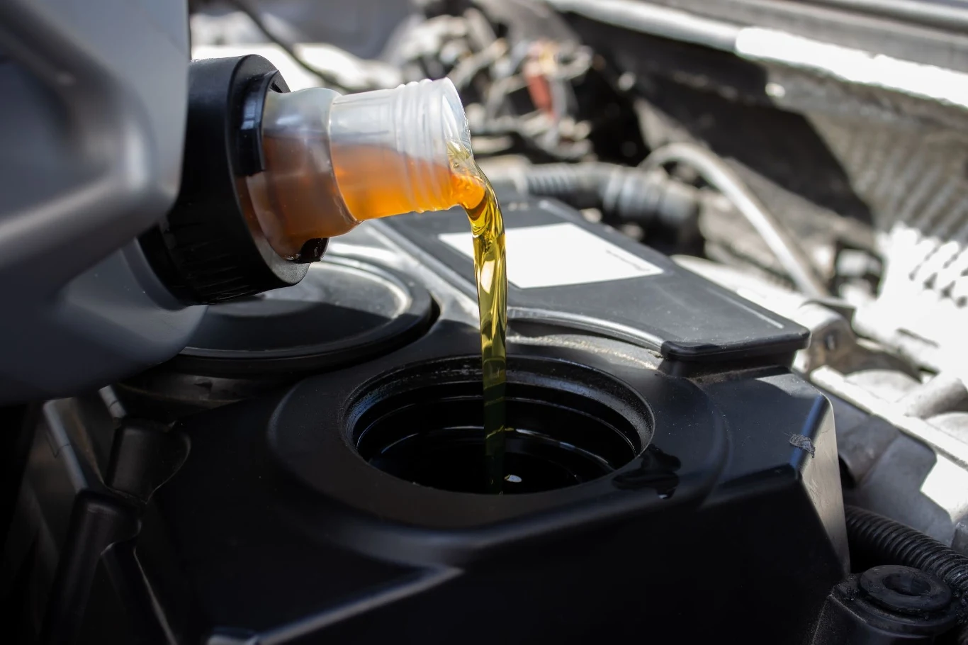 Jeśli olej pachnie w ten sposób, spodziewaj się kłopotów. Nalewanie świeżego oleju silnikowego z butelki do silnika samochodu, widoczny otwór wlewu oraz szczegóły mechaniczne komory silnika.