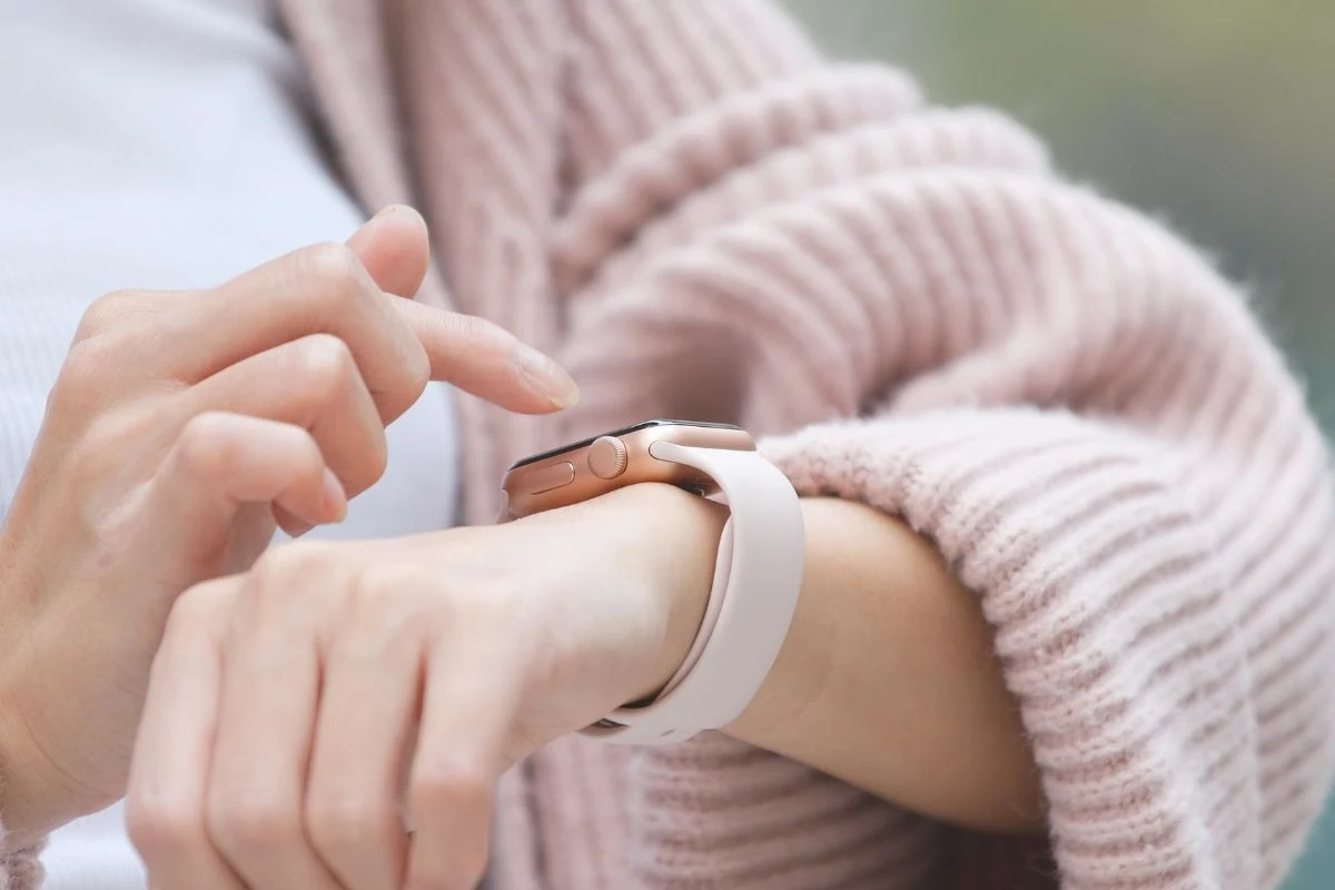 Zbliżenie na rękę osoby korzystającej ze smartwatcha w jasnej opasce, ujęcie eksponuje nowoczesne urządzenie elektroniczne oraz dłoń wskazującą na ekran zegarka.