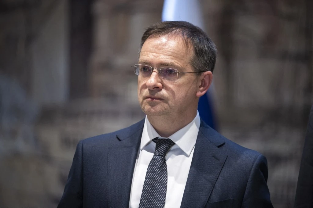 Władimir Medinski zaproponował Ukraińcom spotkanie w celu kontynuacji rozmów pokojowych Mężczyzna w eleganckim garniturze i okularach stoi na tle rozmytego wnętrza z widocznym fragmentem flagi w tle, patrzy poważnym wzrokiem w bok.