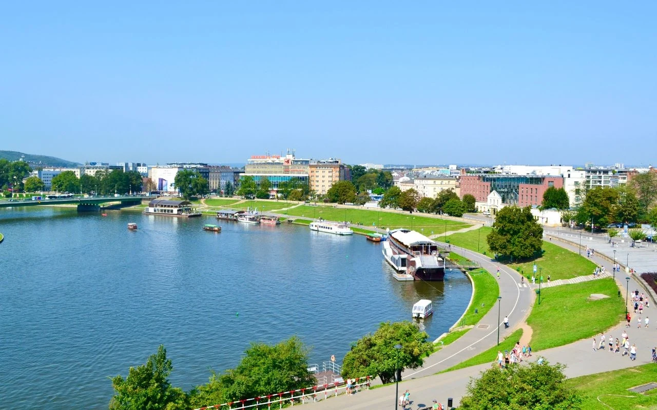 Miasto w Polsce, które kusi wysokimi zarobkami Panorama miasta z rzeką, bulwarami oraz przystanią z kilkoma cumującymi łodziami pasażerskimi, otoczona zabudową miejską i terenami zielonymi, w tle widoczne budynki oraz jasno niebieskie niebo.