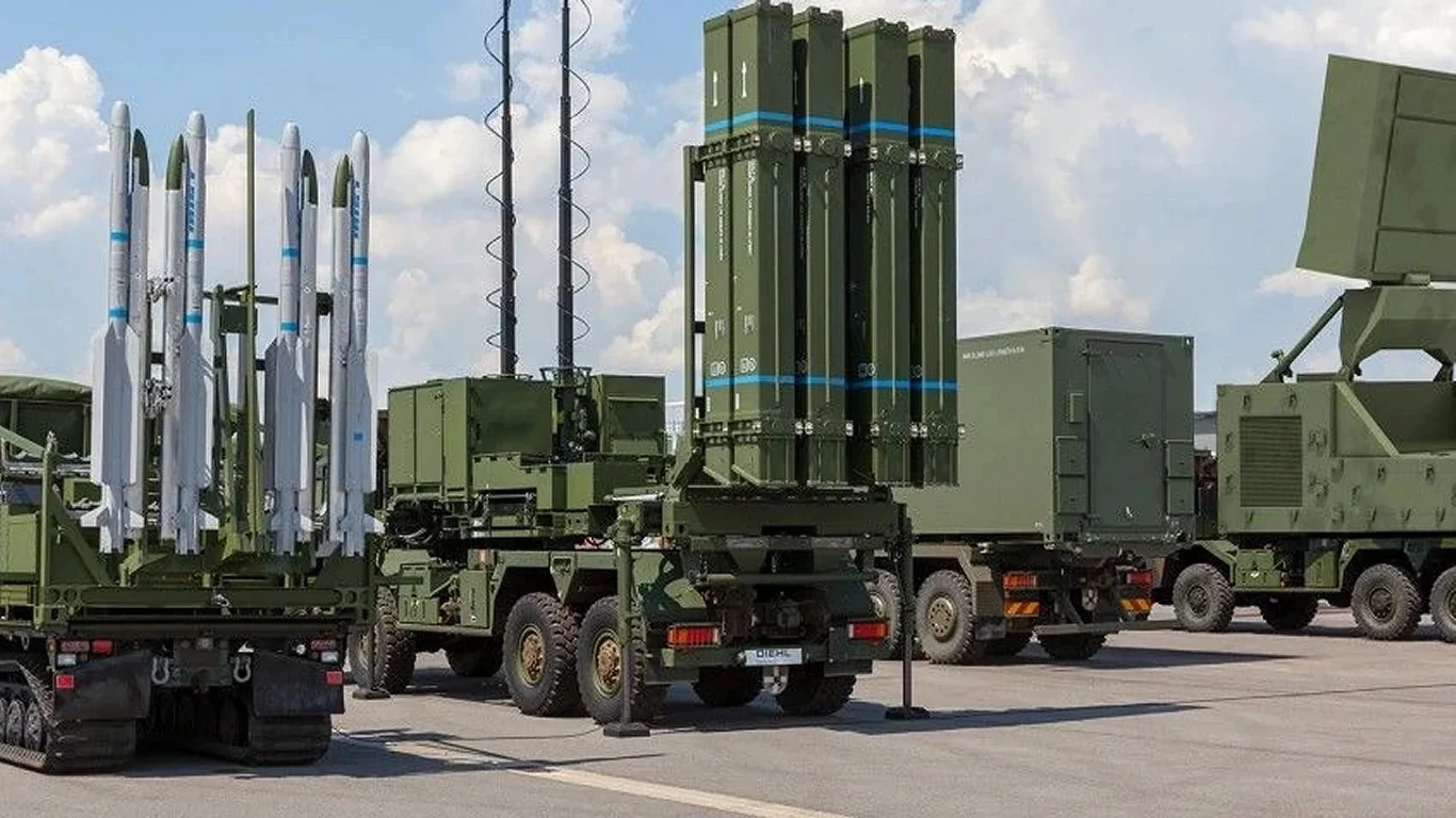 Niemcy ogłosiły gigantyczne wsparcie militarne dla Ukrainy Nowoczesne wojskowe systemy rakietowe i radarowe ustawione w rzędzie na asfalcie, zielone pojazdy wyposażone w wyrzutnie rakiet i zaawansowane anteny, niebo lekko zachmurzone w tle.