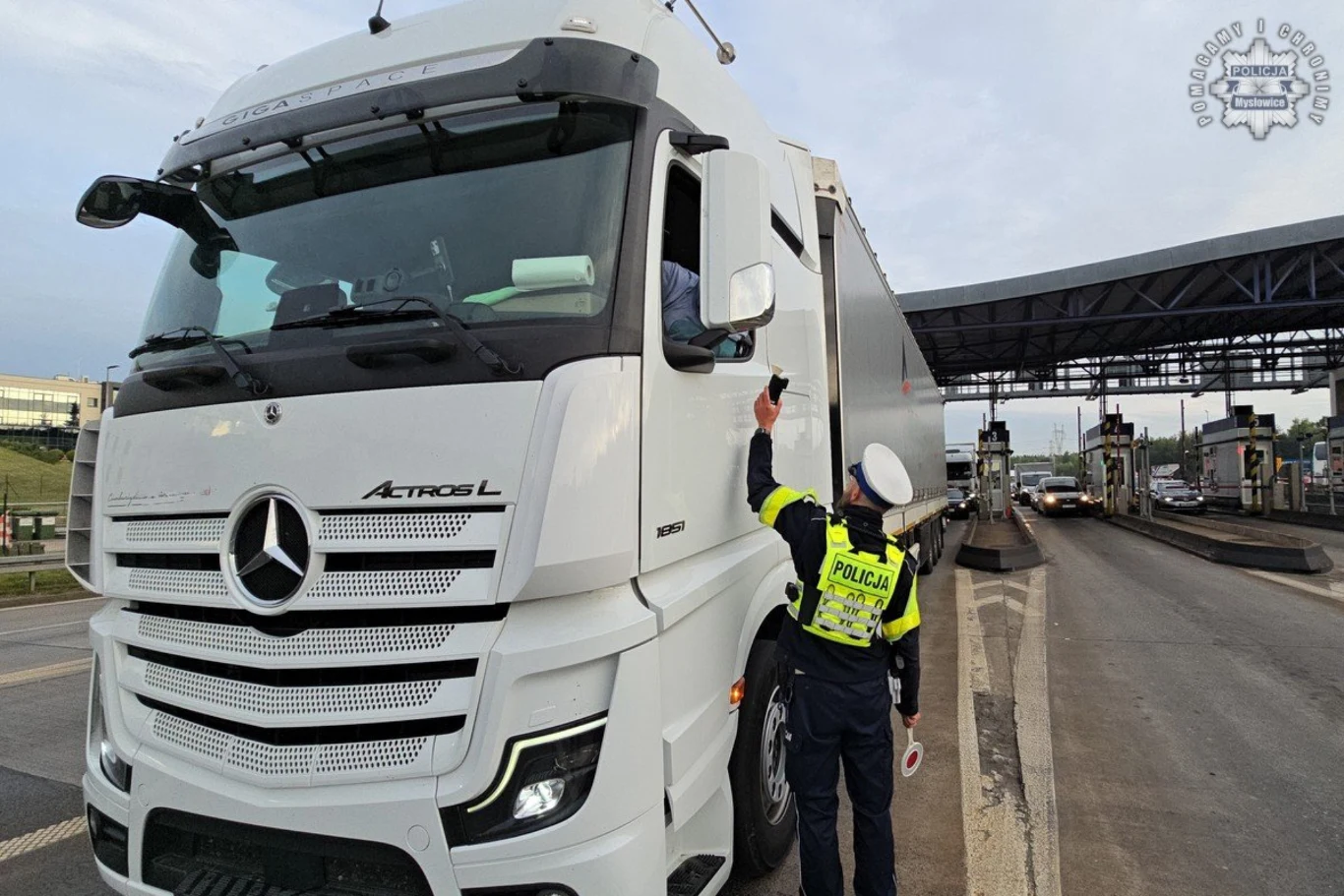 Policjanci przeprowadzili akcję "Trzeźwy poranek" na autostradzie A4. Wpadło siedmiu kierowców. Policjant w odblaskowej kamizelce kontroluje dokumenty kierowcy ciężarówki marki Mercedes Actros L na punkcie kontrolnym przy wjeździe na stację poboru opłat.