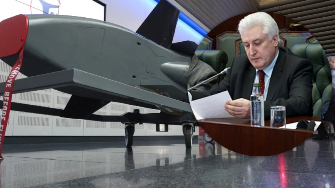 Rosyjski ekspert zagroził Niemcom. Mówi o uderzeniu w kluczową fabrykę Duży dron wojskowy stojący na błyszczącej podłodze w budynku, obok widoczny mężczyzna w garniturze siedzący przy stole i czytający dokumenty, na stole znajdują się butelka wody i szklanka.