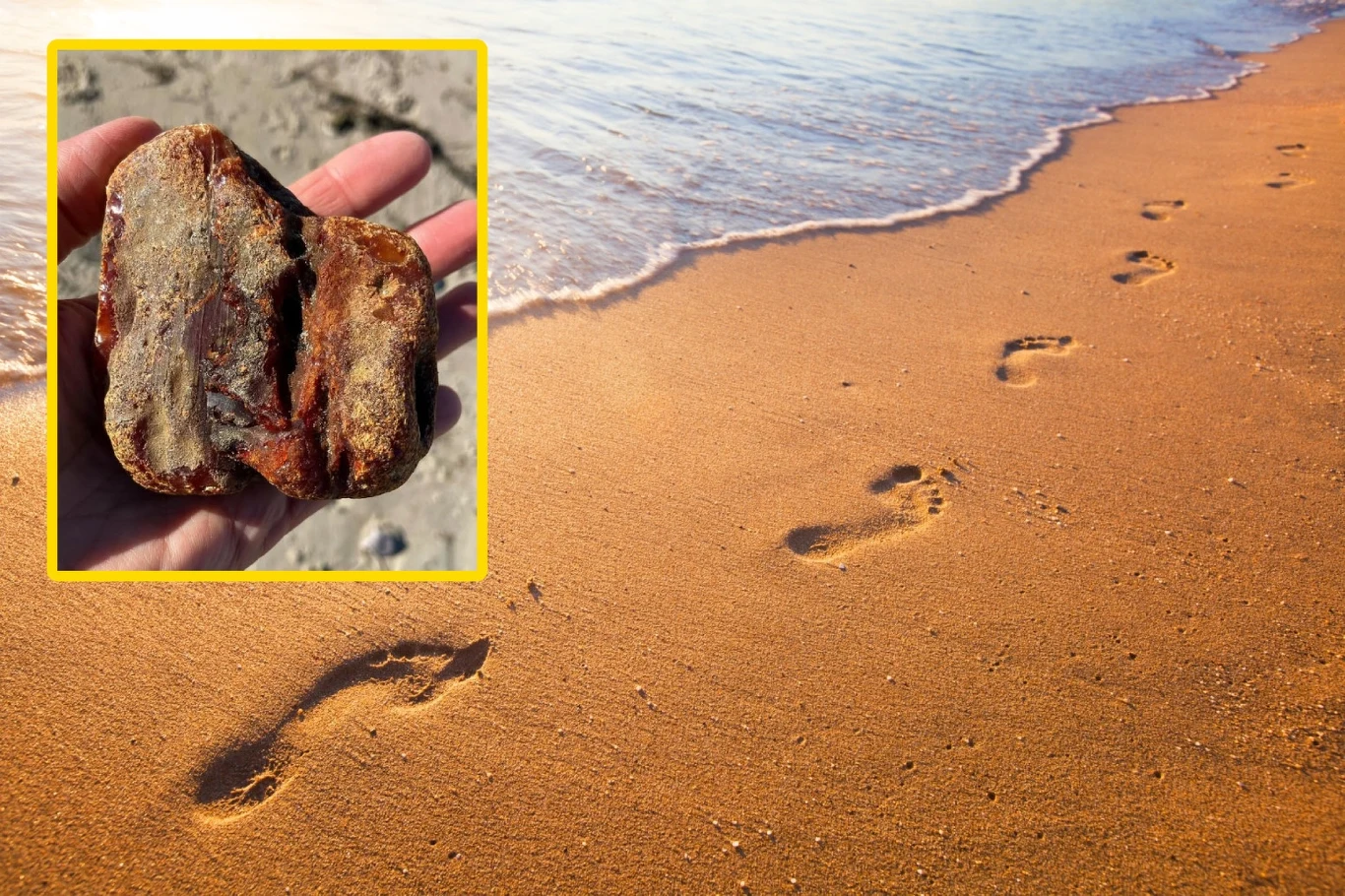 Skarb wyrzucony przez fale Bałtyku. Co można znaleźć na plaży? Plaża z odciśniętymi śladami bosych stóp prowadzącymi w stronę wody, w rogu zdjęcia ręka trzyma dużą bryłę bursztynu wyłowioną z morza.