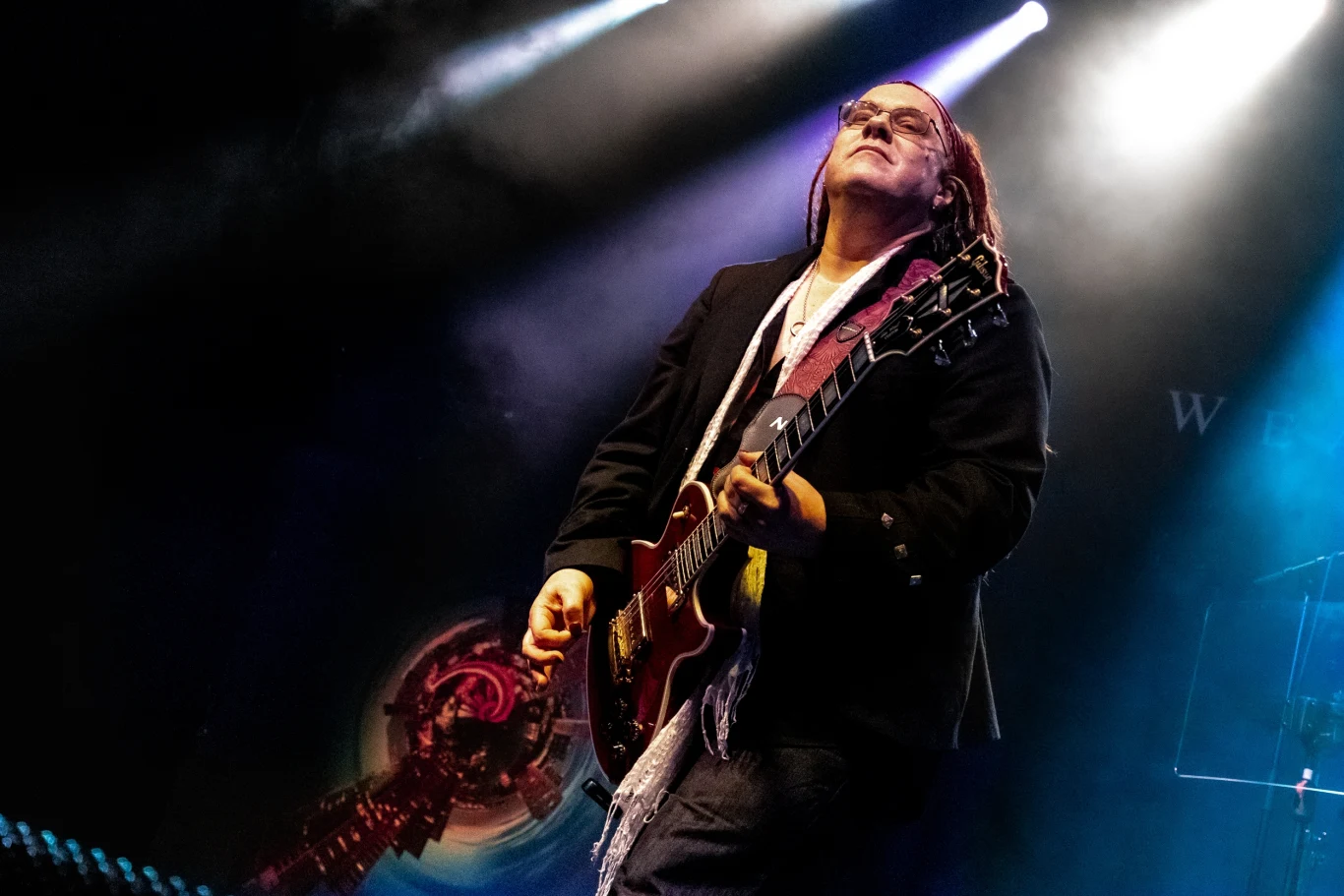 Danny Cavanagh (Weather Systems) w Klubie Studio w Krakowie Muzyk grający na gitarze elektrycznej podczas koncertu, oświetlony kolorowymi reflektorami na scenie, w tle efekty świetlne oraz dym sceniczny.