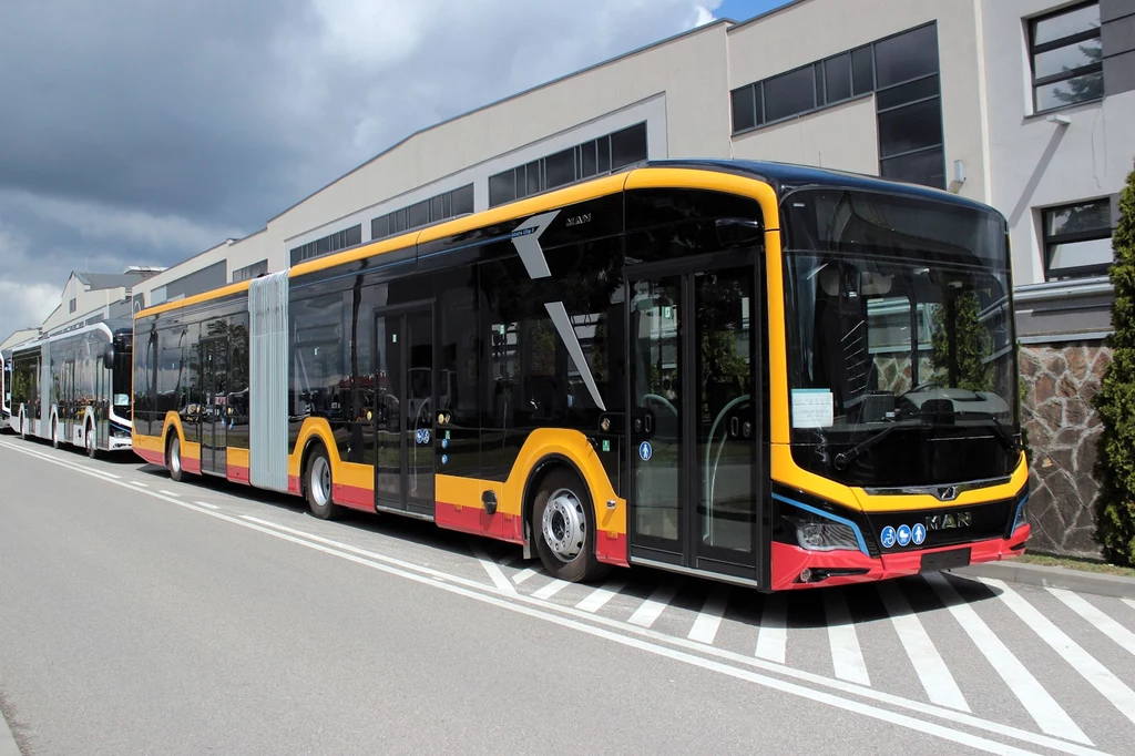 MAN Lion's City na terenie fabryki w Starachowicach Nowoczesny, przegubowy autobus miejskiej komunikacji w żółto-czerwonych barwach stoi zaparkowany wzdłuż ulicy, w tle budynki przemysłowe oraz częściowo zachmurzone niebo.