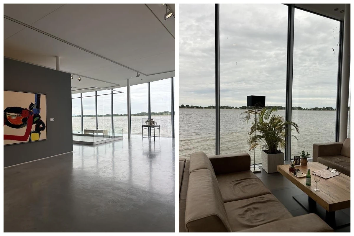 Muzeum sztuki Danubiana pod Bratysławą Nowoczesne wnętrze z dużymi przeszkleniami wychodzącymi na jezioro, po lewej stronie minimalistyczna galeria z abstrakcyjnym obrazem na ścianie, po prawej wygodna część wypoczynkowa z kanapami, rośliną i stolikiem, w tle widok na wodę i naturalny krajo...