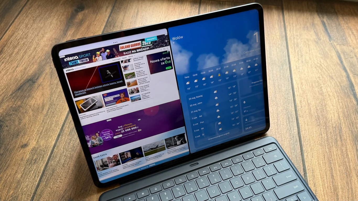 Dużą zaletą OnePlus Pad 3 jest możliwość pracy z aplikacjami na podzielonym ekranie. Tablet z klawiaturą wyświetlający podzielony ekran z otwartą stroną internetową po lewej stronie oraz aplikacją pogodową po prawej, stojący na drewnianej podłodze.