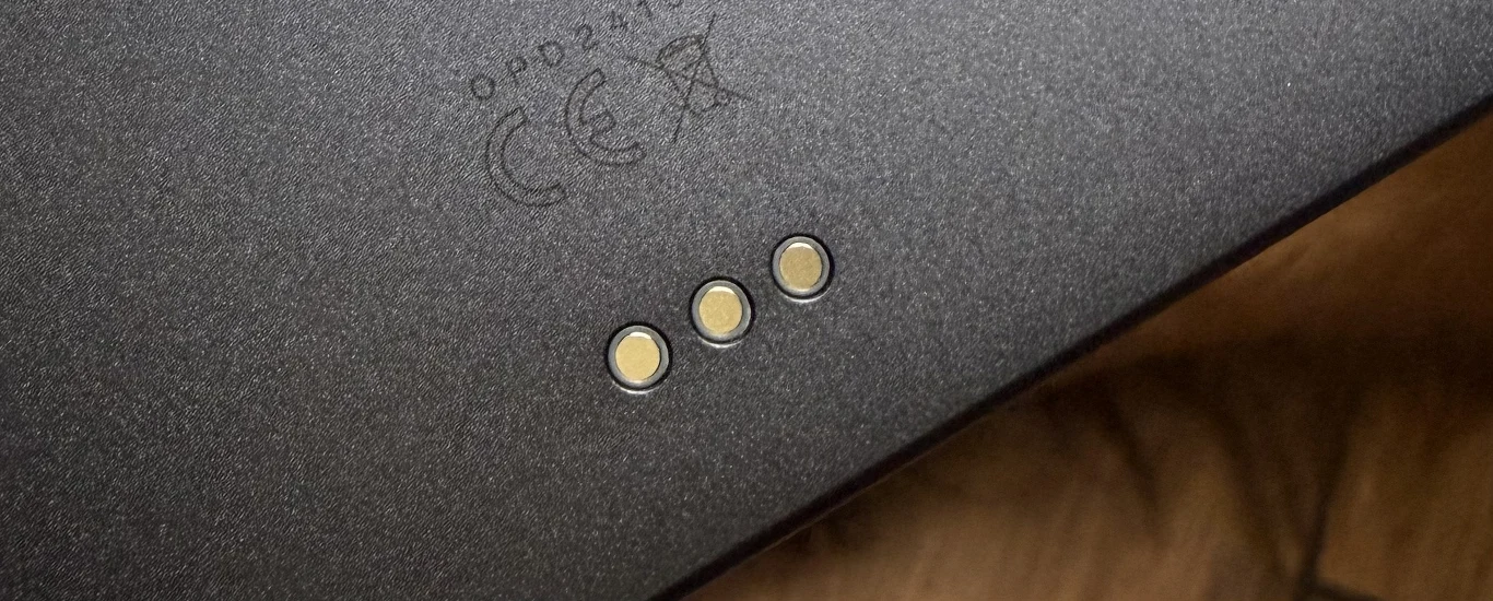 Do komunikacji z akcesoriami używane jest specjalny interfejs. Fragment elektroniki z trzema metalowymi stykami na matowej powierzchni oraz oznaczeniem certyfikatów zgodności CE, widoczna naturalna powierzchnia drewnopodobna w tle.