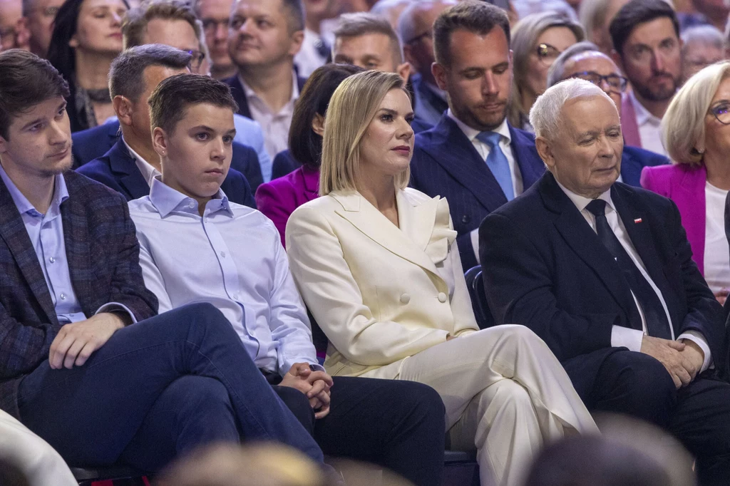 Marta Nawrocka w Łodzi Grupa dorosłych osób i młodzieży siedzi w pierwszym rzędzie na dużym spotkaniu, skupione i elegancko ubrane, w tle widoczne kolejne rzędy obserwujących ludzi.
