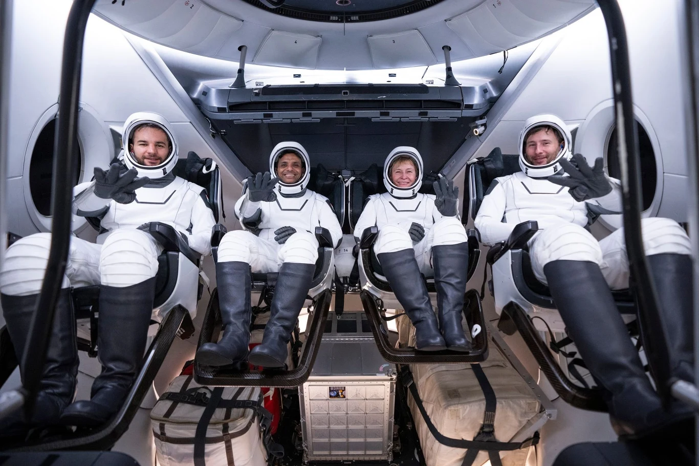 Sławosz Uznański-Wiśniewski i pozostali członkowie załogi Ax-4 w kapsule Crew Dragon firmy SpaceX. Czterech astronautów w nowoczesnych skafandrach siedzi w fotelach we wnętrzu pojazdu kosmicznego, uśmiechają się i machają rękami do obiektywu, otoczeni panelami i sprzętem pokładowym.