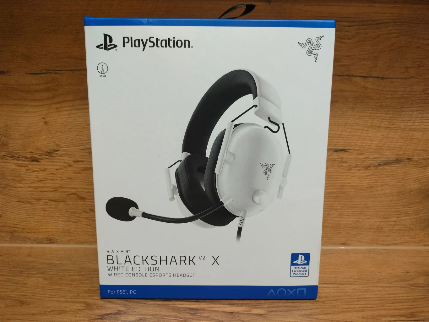 Opakowanie słuchawek gamingowych Razer BlackShark V2 X White Edition z mikrofonem, przeznaczonych do PlayStation 5 i PC, na białym tle z wyraźnym logo PlayStation i Razer.