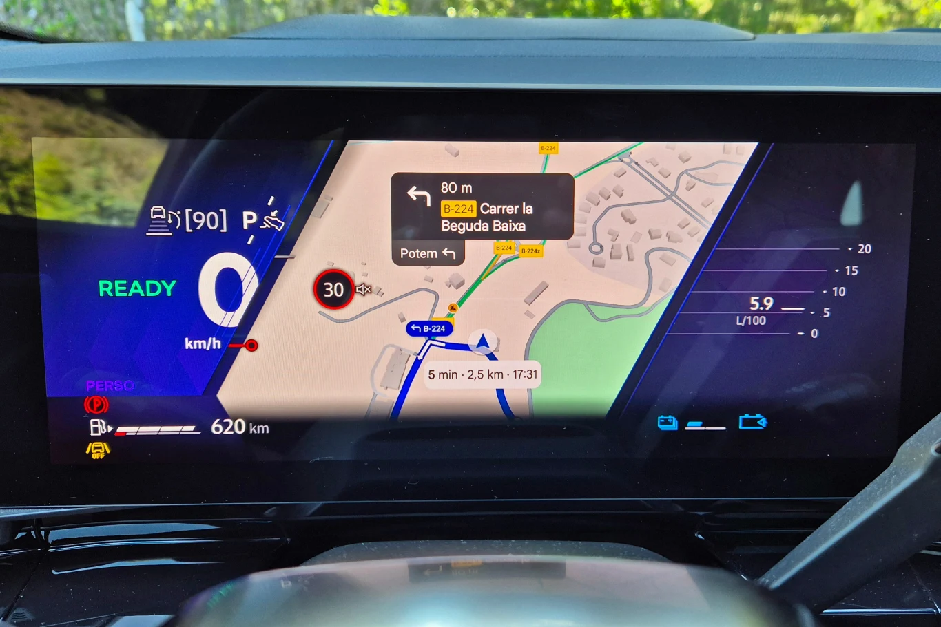 Elektroniczny wyświetlacz samochodowy z widoczną nawigacją GPS, wskazaniami prędkości, zasięgu oraz zużycia paliwa. Na centralnej części ekranu mapa z planowaną trasą, informacją o dojeździe, limitem prędkości i nazwą ulicy.