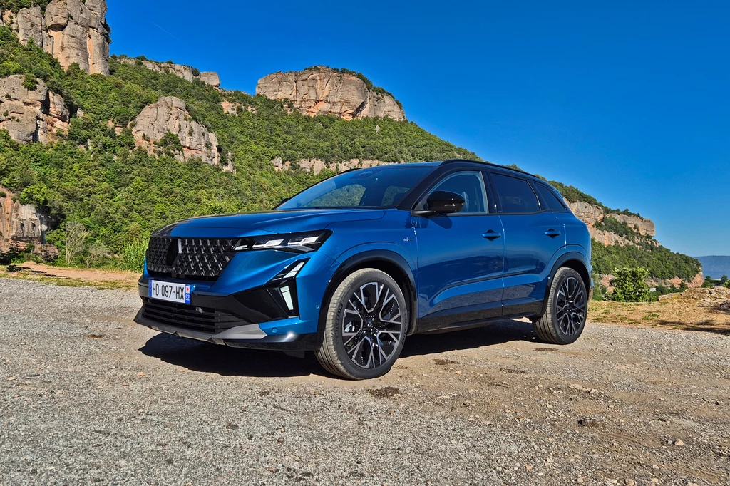 Renault Austral Nowoczesny, niebieski SUV zaparkowany na tle skalistych wzgórz oraz zieleni, samochód wyróżnia się sportowym wyglądem, dużymi felgami i charakterystycznym grillem, na horyzoncie błękitne niebo.
