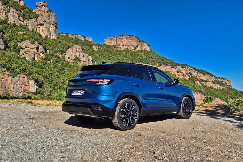 Renault Austral Niebieski samochód typu SUV zaparkowany na żwirowej drodze na tle skalistego wzgórza porośniętego zielenią, pod czystym niebem.