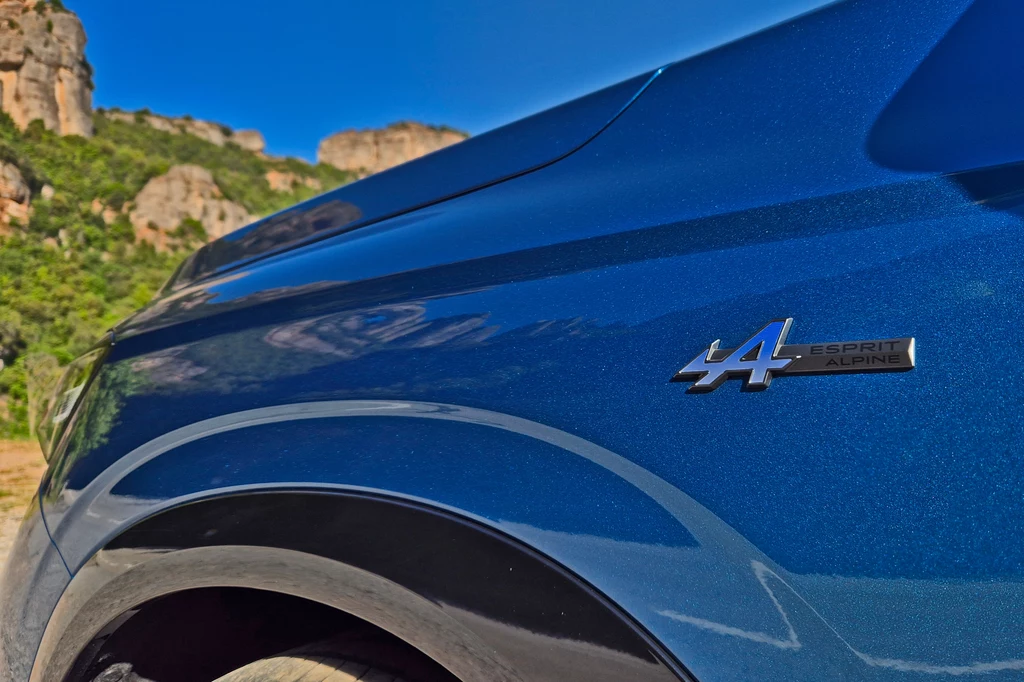 Renault Austral Błyszczący bok niebieskiego samochodu z emblematem 44 Esprit Alpine na tle gór i nieba.