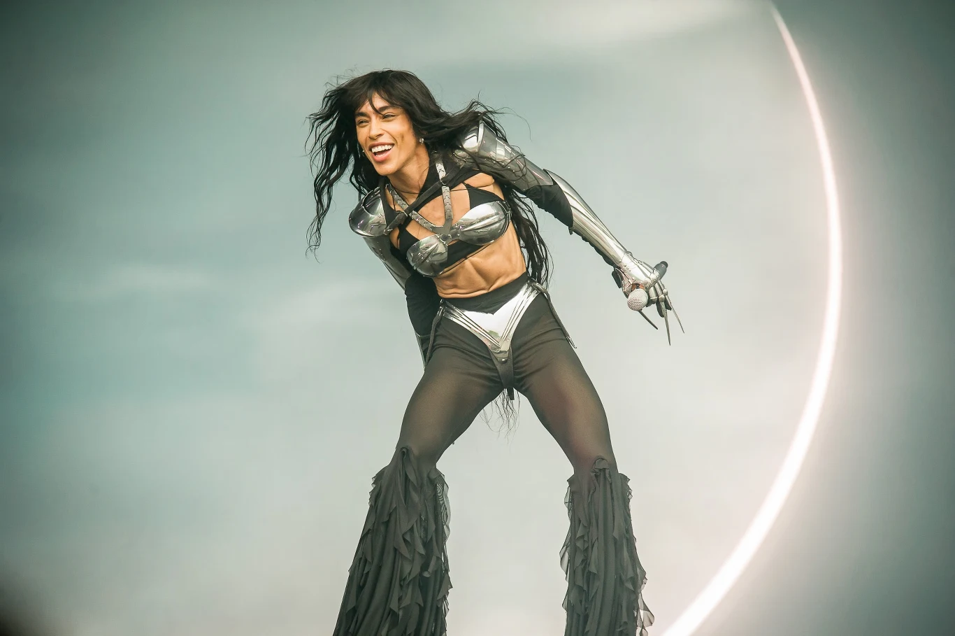 Loreen na Orange Warsaw Festival 2025 Artystka w futurystycznym kostiumie scenicznym śpiewa na scenie, dynamiczna poza oraz efektowna stylizacja w metalicznych barwach przyciągają uwagę, w tle jasny półokrąg przypominający księżyc.