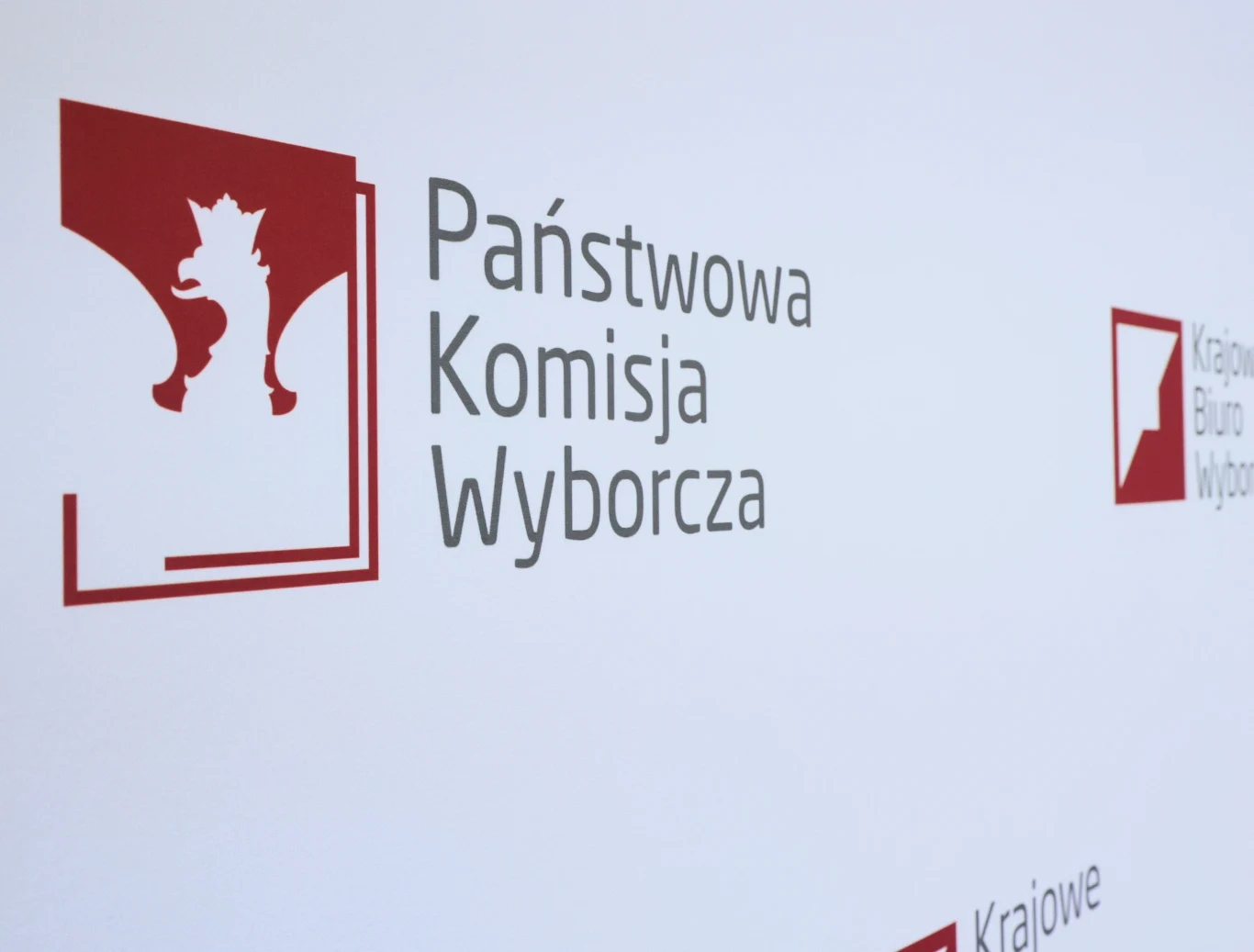Wybory prezydenckie 2025 - druga tura. Kiedy pierwsza konferencja PKW? Logo Państwowej Komisji Wyborczej na jasnym tle, po lewej stronie czerwony kwadrat z białym orłem, obok szare napisy z nazwą instytucji.