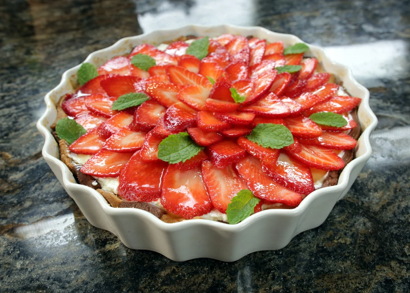 Tarta z truskawkami Tarta z truskawkami na kruchym spodzie, udekorowana świeżymi listkami mięty, ułożona na ciemnym, kamiennym blacie.