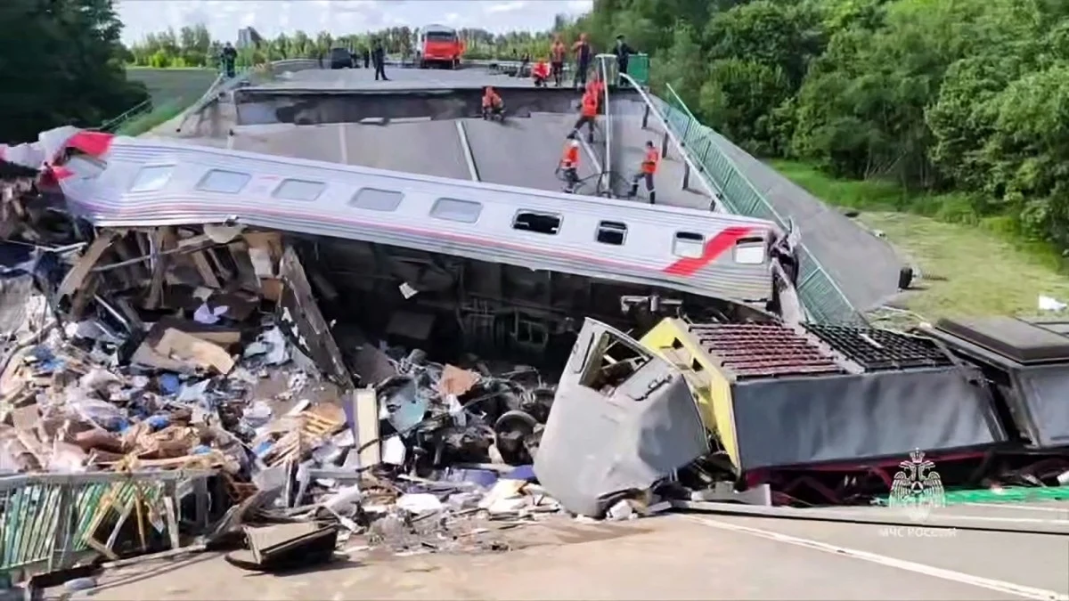 W nocy z soboty na niedzielę w Rosji doszło do zawalenia się dwóch mostów Zawalony most z rozbitym pociągiem osobowym leżącym na gruzach, wokół rozrzucone fragmenty wagonów i rzeczy osobiste, ratownicy w pomarańczowych kamizelkach pracują na zniszczonej infrastrukturze mostu, wokół widoczne drzewa i zieleń.