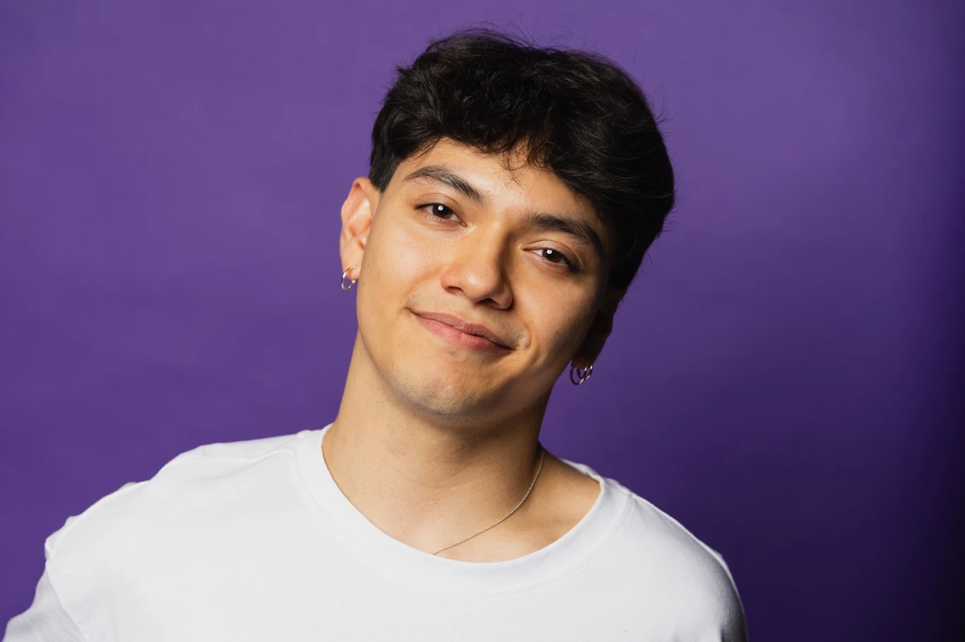 JJ - zwycięzca Eurowizji mówi o swojej polskiej rodzinie w "halo tu Polsat" Młody mężczyzna z krótkimi, ciemnymi włosami uśmiecha się subtelnie, ubrany w białą koszulkę na tle gładkiego fioletowego tła.