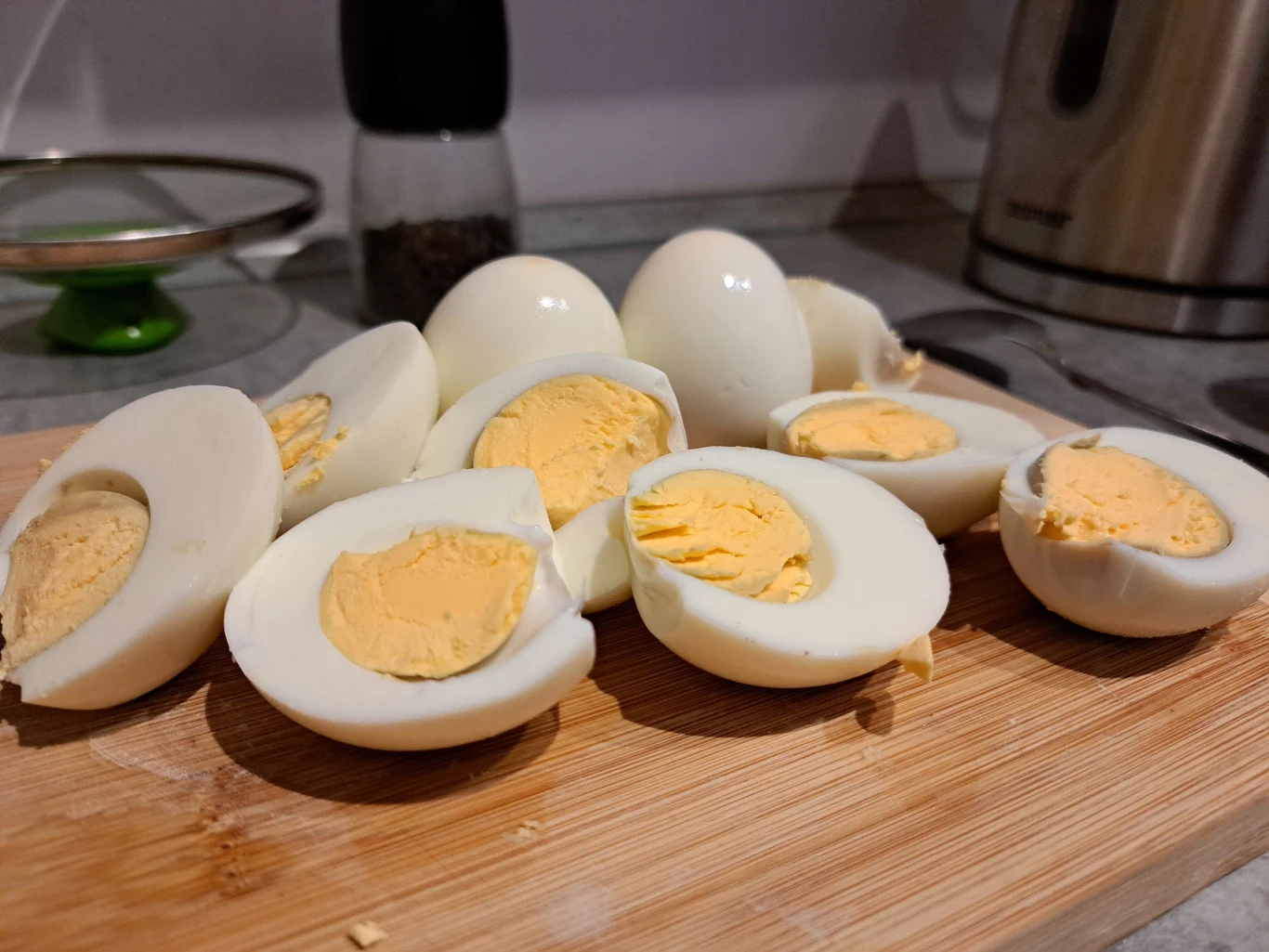 Gotowanie jajek to jedna z najprostszych czynności wykonywanych w kuchni, a jednak potrafi sprawić problemy. Trzeba wiedzieć, jakich błędów unikać. Pokrojone na pół jajka na twardo ułożone na drewnianej desce do krojenia na kuchennym blacie, w tle widoczne przybory kuchenne.