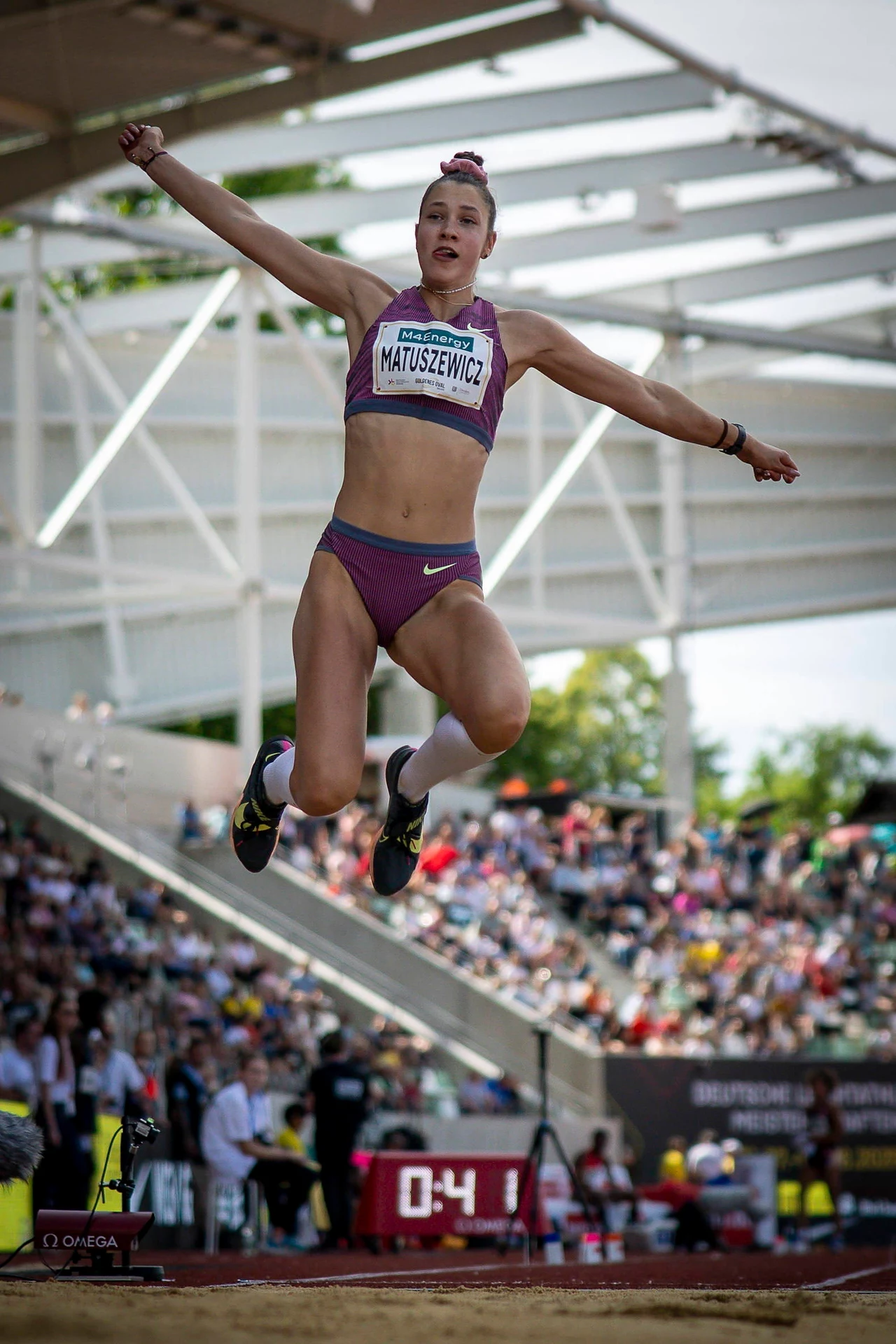 Anna Matuszewicz w Dreźnie Zawodniczka w stroju sportowym wykonuje skok w dal na stadionie lekkoatletycznym, w tle widoczni kibice oraz sędziowie, całość odbywa się podczas zawodów na świeżym powietrzu.