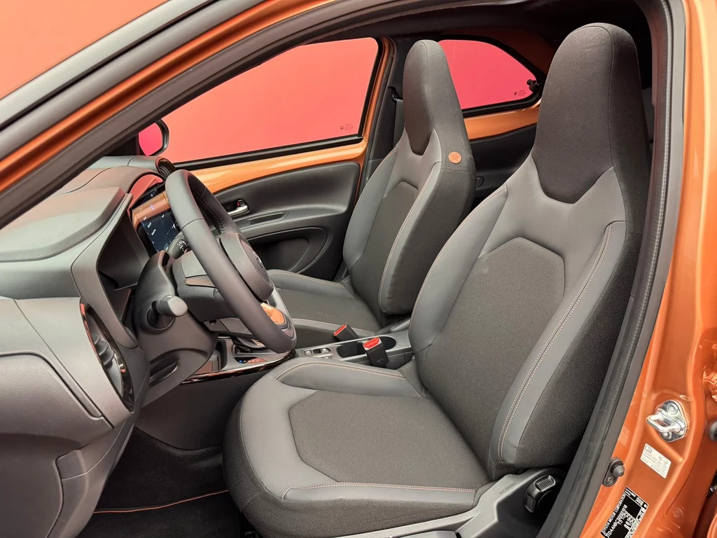 Nowe Aygo X korzysta z kompleksowego pakietu systemów bezpieczeństwa i wsparcia kierowcy Toyota Safety Sense Wewnątrz nowoczesnego samochodu znajdują się dwa komfortowe fotele przednie, deska rozdzielcza z panelem sterowania oraz elegancka kierownica, całość utrzymana w czarno-pomarańczowej kolorystyce.