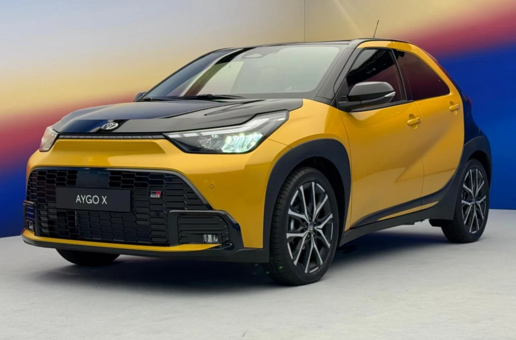 Toyota Aygo w wersji GR SPORT wyróżnia się lakierem i sportowymi akcentami. Nowoczesny, miejski samochód Toyota Aygo X w dwukolorowym żółto-czarnym nadwoziu, sportowe felgi, charakterystyczny grill oraz designerskie reflektory LED, auto ustawione na jasnym tle z gradientem kolorystycznym.