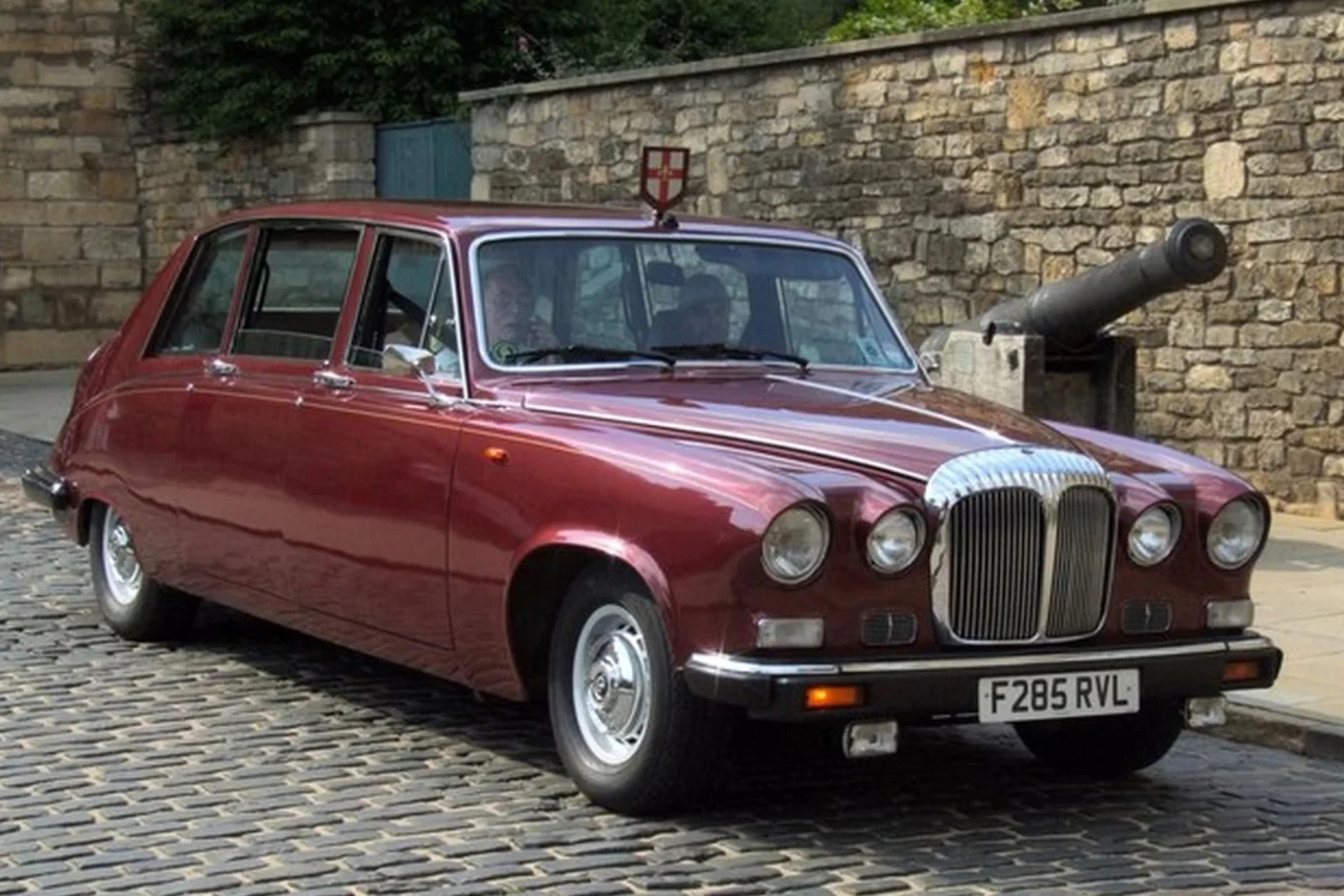 Daimler DS240 - Jeździły w nim głowy państw, a także Freddie Mercury. Klasyczny, bordowy samochód osobowy marki Daimler DS420 zaparkowany na brukowanej ulicy obok kamiennego muru i starej armaty.