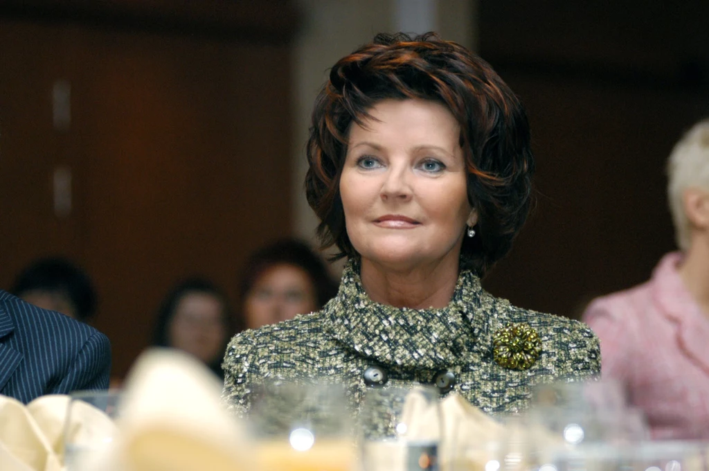 Jolanta Kwaśniewska zaskoczyła Polaków pozytywnie w roli Pierwszej Damy Kobieta o ciemnych, falowanych włosach w eleganckim ubraniu siedzi przy stole podczas oficjalnego spotkania, tło rozmyte, widać innych uczestników wydarzenia.