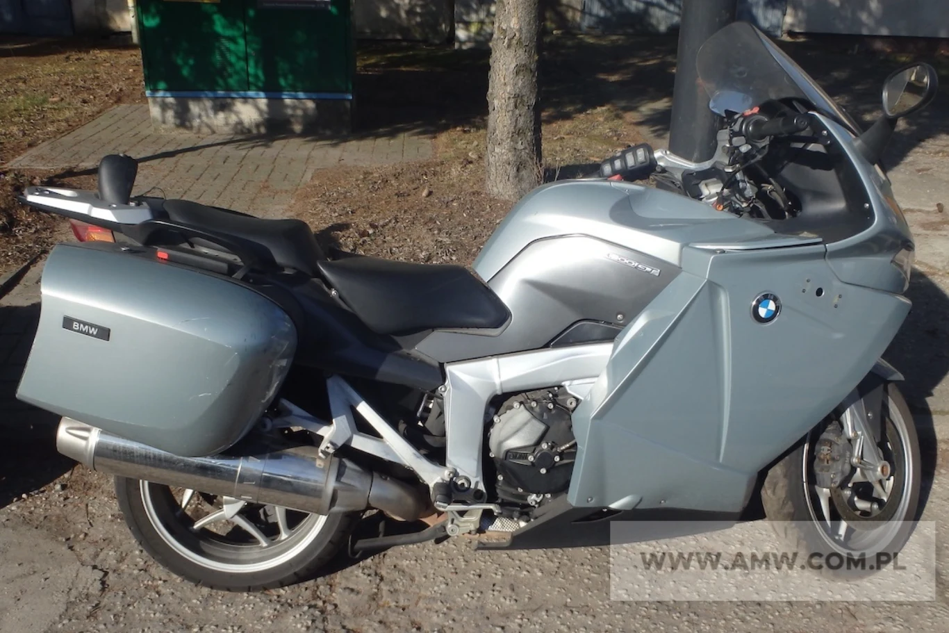 Szosowo-turystyczny GT zdaje się być w najlepszym stanie. Wymaga niewielkich poprawek wizualnych. Srebrny motocykl marki BMW z bocznymi kuframi bagażowymi stoi zaparkowany na chodniku w słoneczny dzień, w tle widoczne drzewo oraz fragment trawnika.