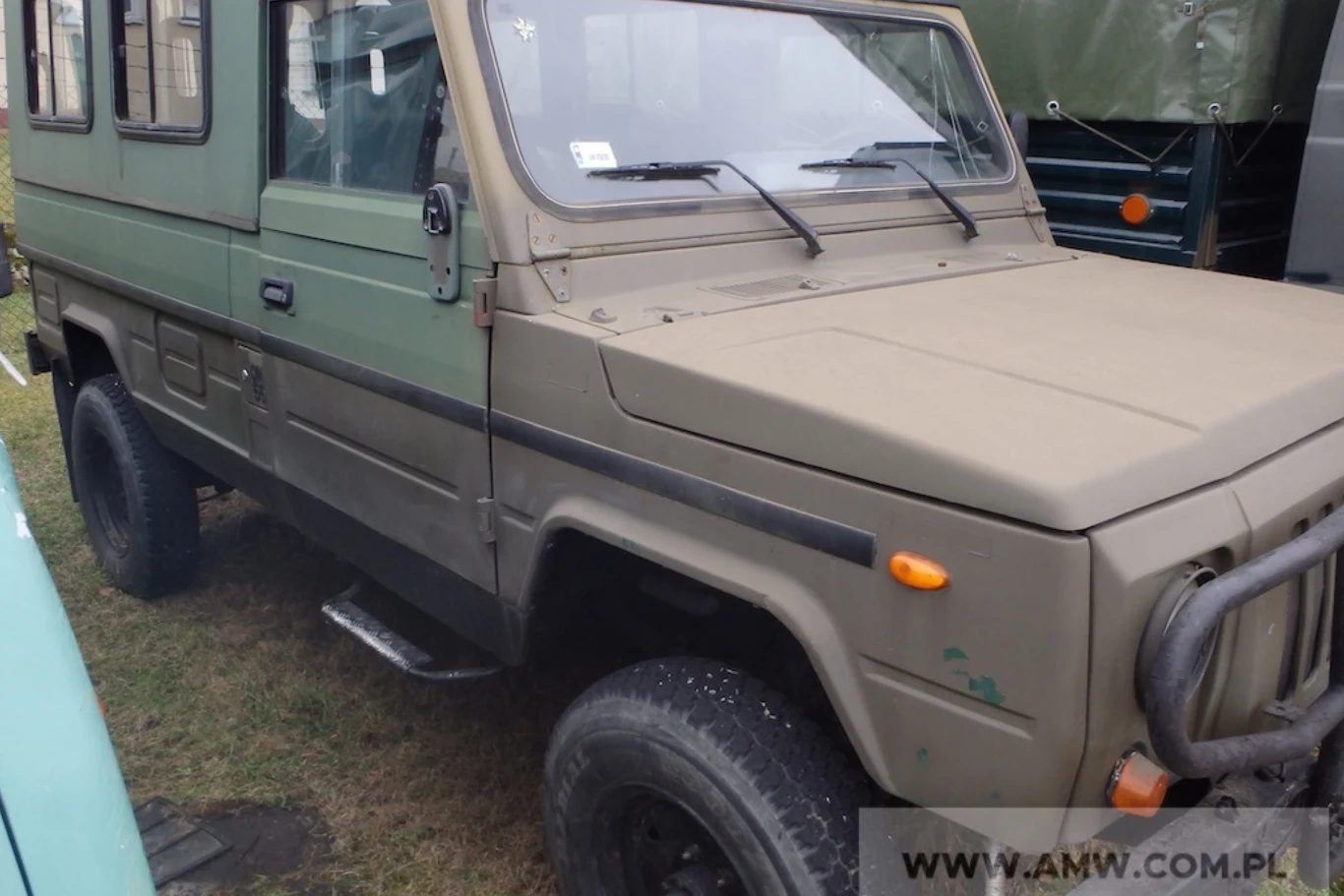 Tarpan Honker to kontrowersyjny samochód. Wielu twierdzi, że to najgorsze auto produkowane w Polsce. Zielony pojazd terenowy o wojskowym wyglądzie, solidna kratka ochronna na przednim zderzaku, zabudowana kabina z bocznymi oknami, pojazd stoi na trawie obok innych pojazdów.