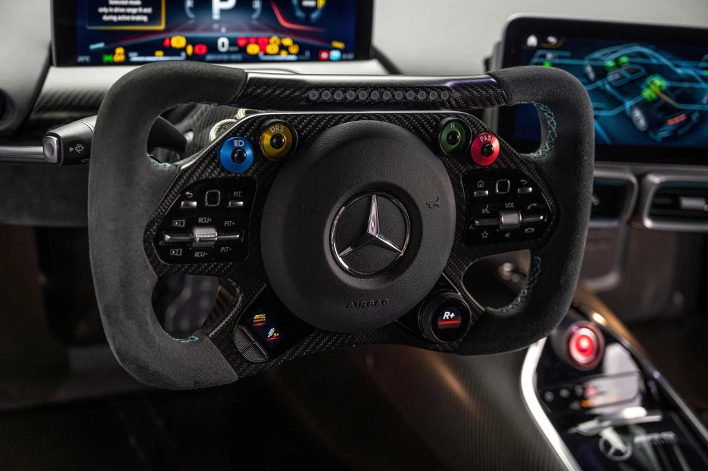 Wewnątrz faktycznie Mercedes-AMG One przypomina bolid Formuły 1 Kierownica bolidu wyścigowego Mercedes AMG z przyciskami funkcyjnymi oraz ekranami pokazującymi dane telemetryczne i ustawienia pojazdu, wnętrze nowoczesnego samochodu sportowego.