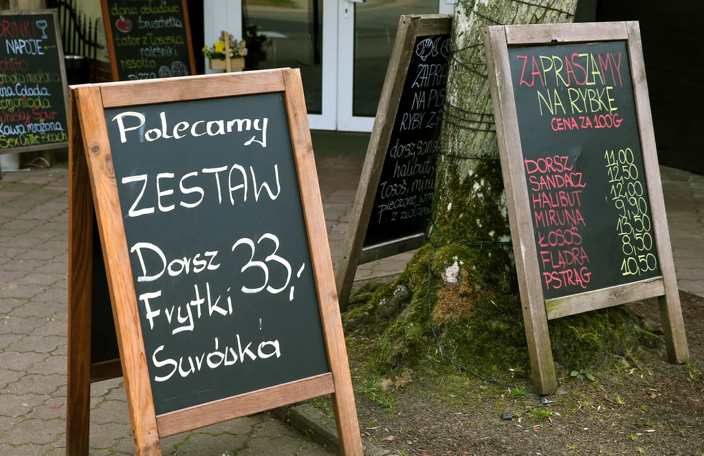 Ceny zestawów obiadowych nad Bałtykiem mogą znacząco się od siebie różnić Tablice z menu restauracji ustawione na zewnątrz, zapisane kredą oferty dnia oraz ceny różnych dań rybnych, głównym elementem jest informacja o zestawie: dorsz, frytki, surówka za 33 zł.