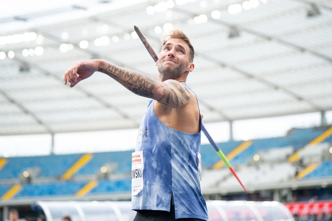 Marcin Krukowski Lekkoatleta podczas rzutu oszczepem na stadionie, w tle trybuny i zadaszenie obiektu sportowego.