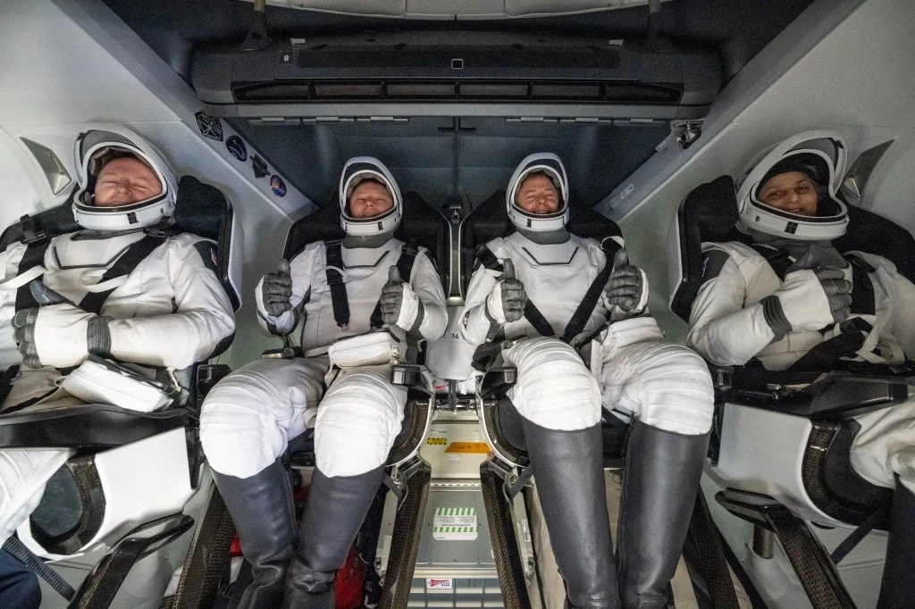 Z powodu usterki kilkudniowa misja zmieniła się w dziewięciomiesięczną (fot. NASA) Czterech astronautów w białych skafandrach siedzi w kapsule kosmicznej na fotelach startowych, przygotowując się do misji. Ich twarze są osłonięte przez szybki w kaskach, a wnętrze kapsuły wypełniają panele sterowania i elementy technologiczne.