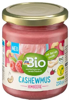 Ostrzeżenie GIS dotyczące musu Słoik dmBio Cashewmus Himbeere o pojemności 250 g z różowym kremem z nerkowców i malin, etykieta informuje o składzie wegańskim i certyfikacie bio, na etykiecie widoczne grafiki malin i orzechów nerkowca.